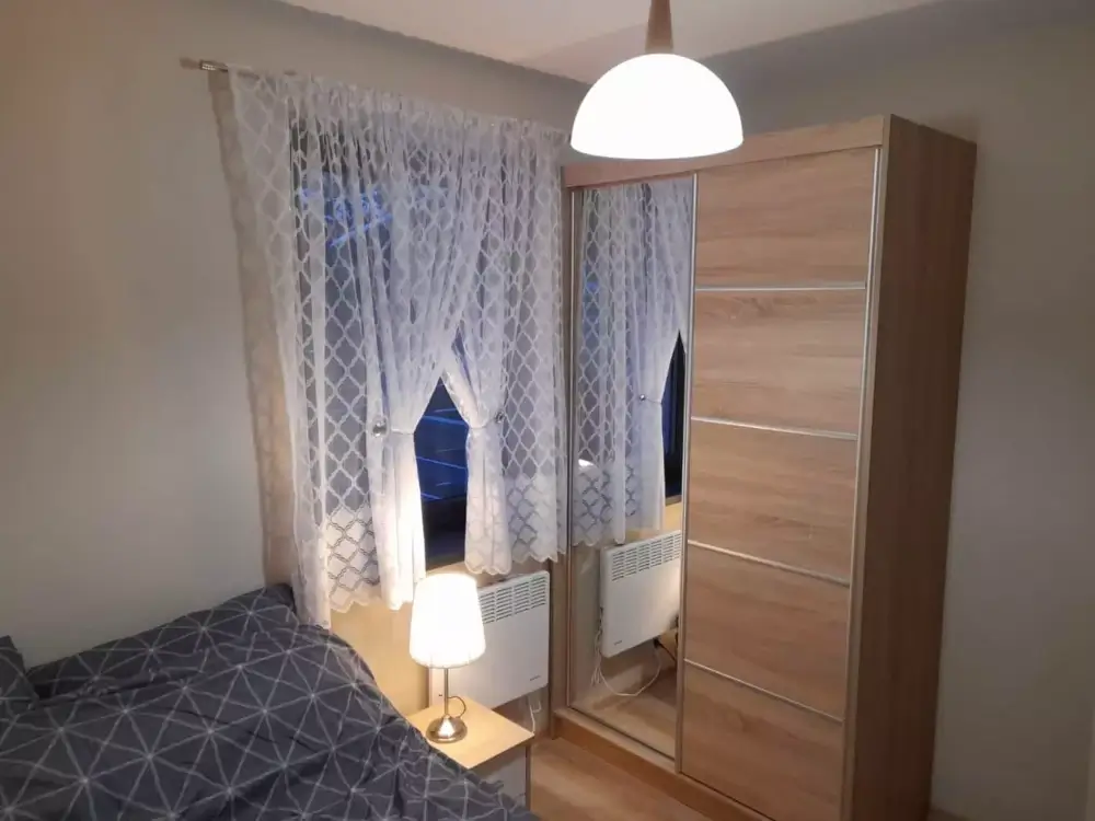 Przytulna sypialnia z funkcjonalną szafą i oknem z widokiem na las